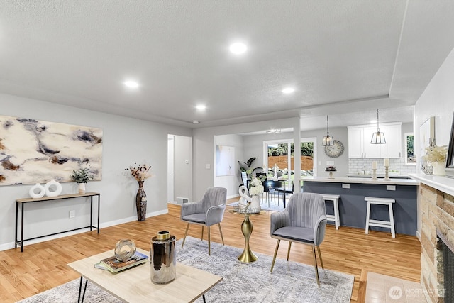 living room featuring a textured ceiling, light wood finished floors, baseboards, and recessed lighting