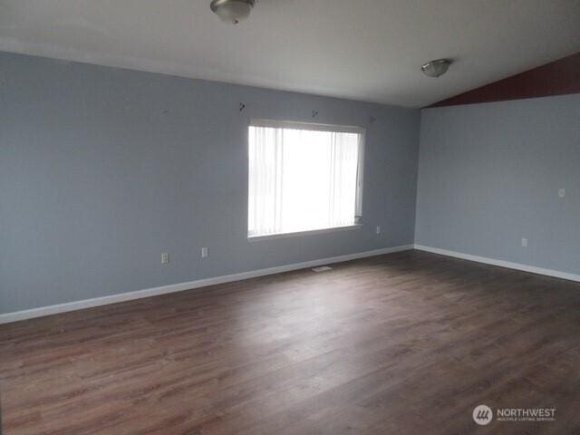 spare room featuring baseboards, vaulted ceiling, and dark wood finished floors