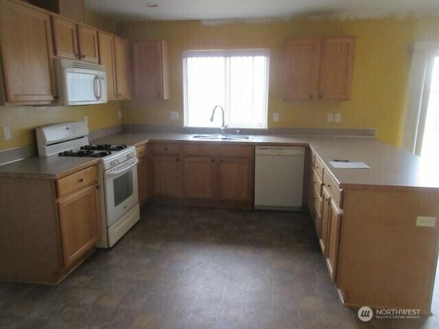 kitchen with a peninsula, white appliances, light countertops, and a sink