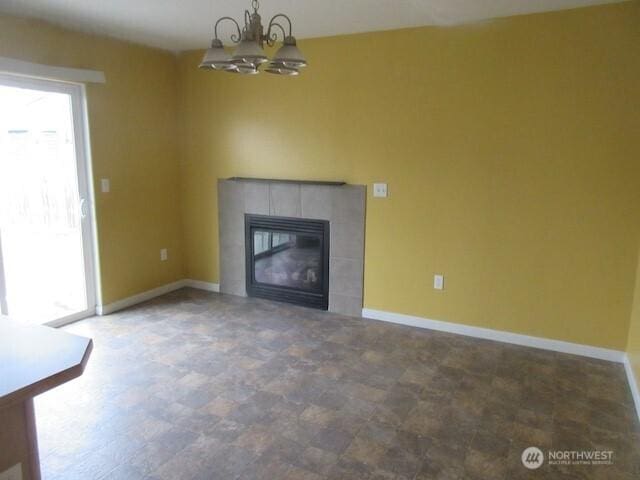 unfurnished living room featuring a notable chandelier, a tile fireplace, and baseboards