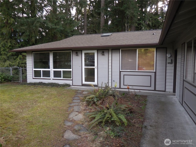 entrance to property with a shingled roof, a lawn, and fence