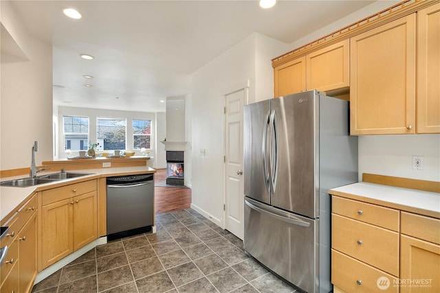 kitchen featuring light brown cabinets, recessed lighting, a sink, appliances with stainless steel finishes, and a glass covered fireplace