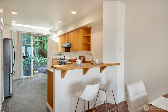 kitchen featuring a breakfast bar area, under cabinet range hood, stainless steel appliances, a peninsula, and open shelves