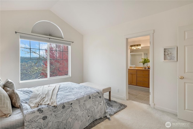 bedroom featuring lofted ceiling, ensuite bath, baseboards, and light colored carpet