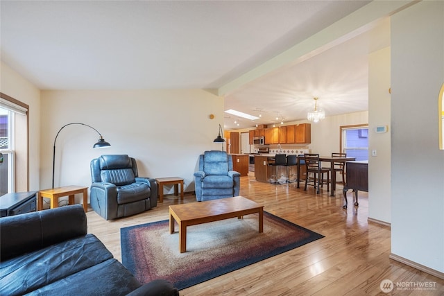 living room with lofted ceiling with beams, light wood finished floors, an inviting chandelier, and baseboards