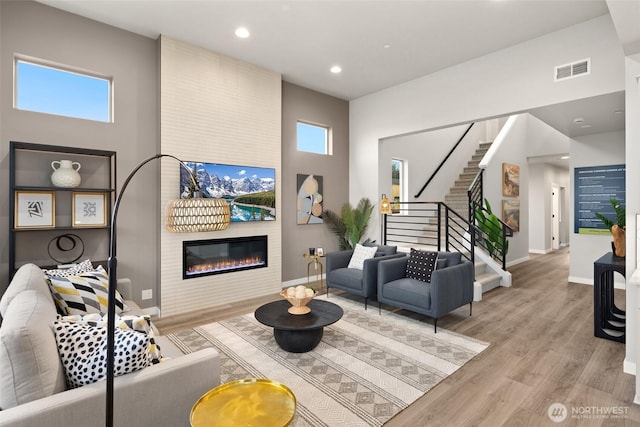 living room featuring a large fireplace, visible vents, stairway, light wood-type flooring, and plenty of natural light