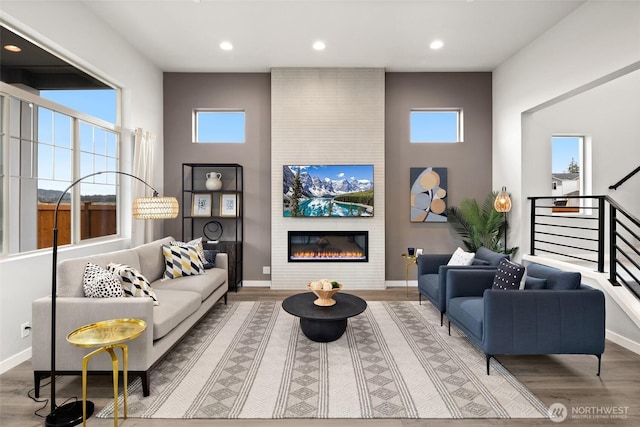 living area with a large fireplace, stairway, light wood-style flooring, and baseboards