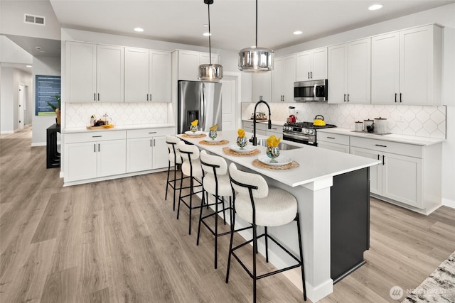 kitchen featuring visible vents, appliances with stainless steel finishes, a breakfast bar, light wood-style floors, and a sink