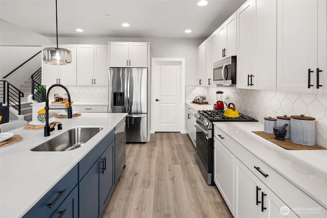 kitchen featuring blue cabinetry, appliances with stainless steel finishes, white cabinets, and a sink