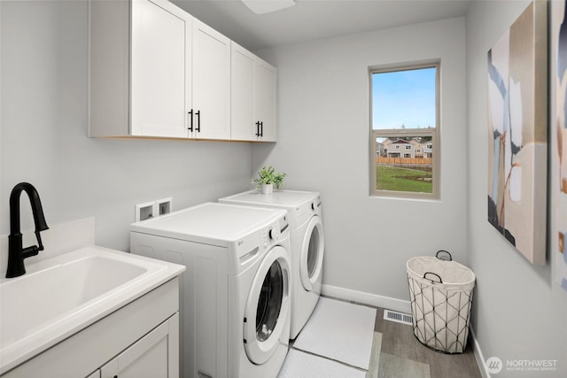 laundry area with cabinet space, visible vents, wood finished floors, washer and dryer, and a sink