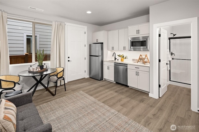 kitchen with visible vents, stainless steel appliances, light wood-type flooring, white cabinetry, and a sink