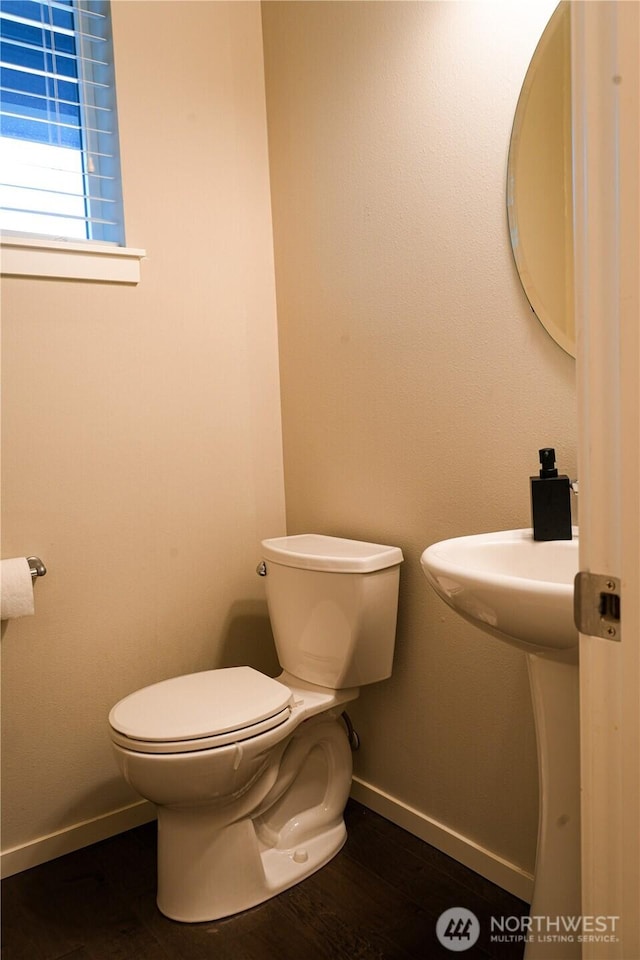 half bathroom with wood finished floors, toilet, and baseboards