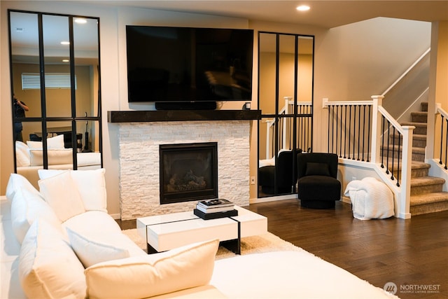 living area featuring a stone fireplace, stairway, wood finished floors, and recessed lighting