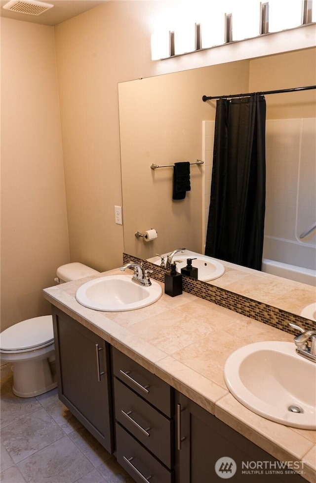 full bathroom with double vanity, a sink, and toilet