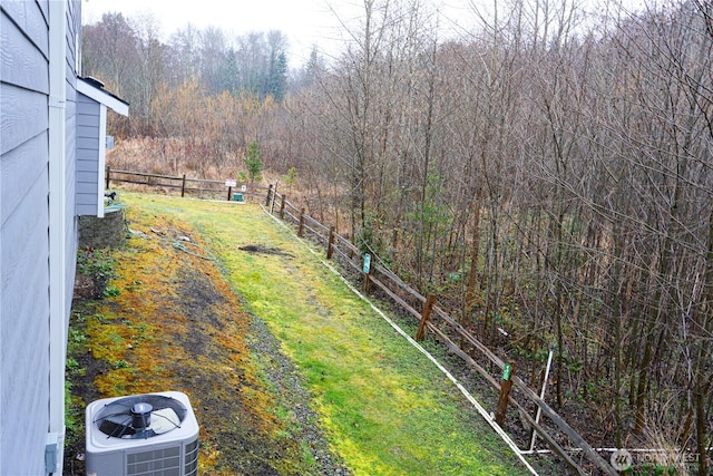 view of yard featuring a view of trees, fence, and central AC