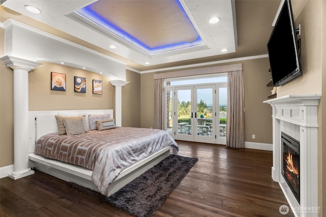 bedroom with wood finished floors, access to outside, ornamental molding, a tray ceiling, and ornate columns