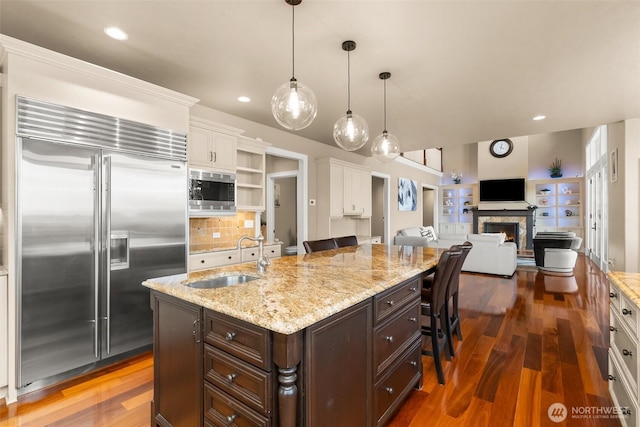 kitchen with built in appliances, dark brown cabinetry, a sink, a kitchen breakfast bar, and white cabinets