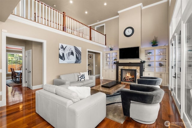 living area with baseboards, a towering ceiling, ornamental molding, wood finished floors, and a lit fireplace