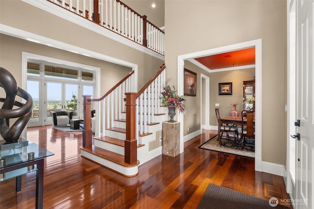 stairs featuring crown molding, a towering ceiling, baseboards, and wood finished floors