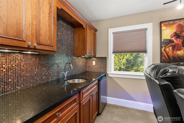 kitchen featuring a sink, baseboards, decorative backsplash, dishwasher, and dark stone countertops