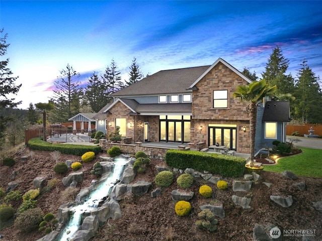 back of house at dusk featuring stone siding, a patio, and fence