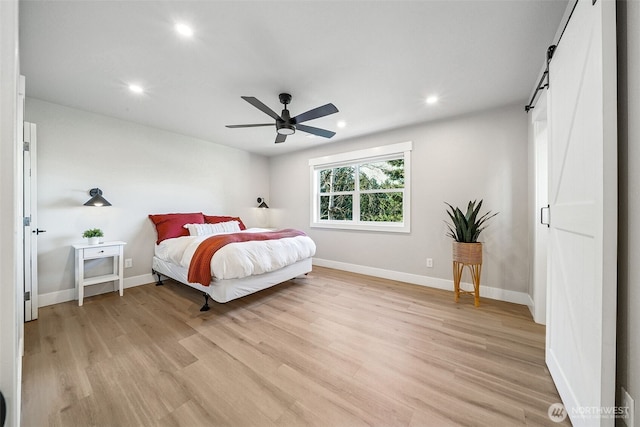 bedroom featuring light wood finished floors, recessed lighting, a barn door, a ceiling fan, and baseboards