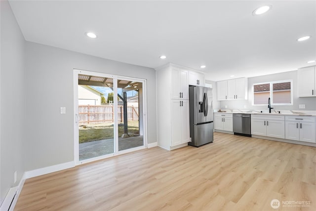 kitchen featuring light wood finished floors, stainless steel appliances, light countertops, white cabinetry, and a sink