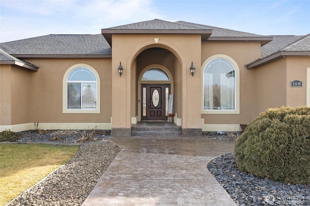 view of exterior entry featuring roof with shingles and stucco siding