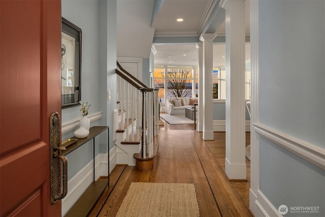 hallway featuring wood finished floors, baseboards, stairway, decorative columns, and crown molding