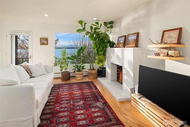 living room with light wood-style floors, a baseboard radiator, a fireplace with raised hearth, and recessed lighting