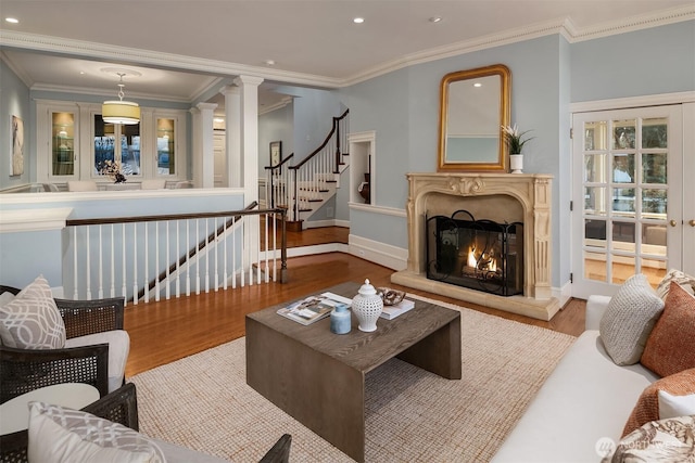 living room featuring a warm lit fireplace, wood finished floors, decorative columns, and crown molding