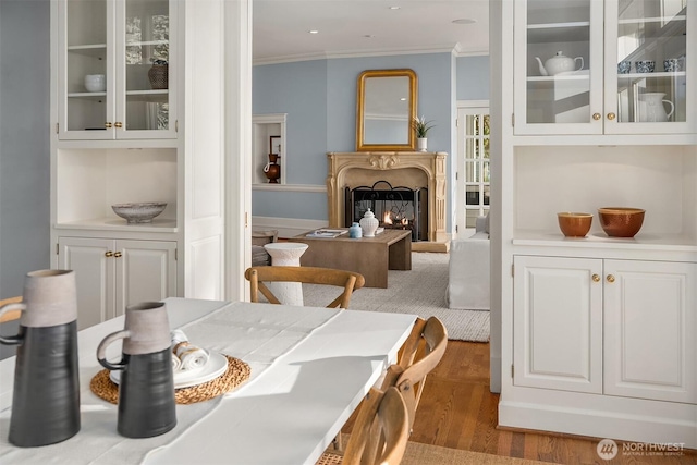 dining area with ornamental molding, recessed lighting, a warm lit fireplace, and wood finished floors