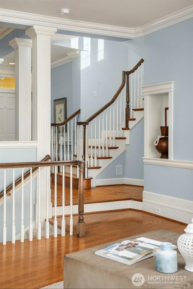 stairway featuring ornamental molding, wood finished floors, decorative columns, and baseboards