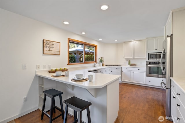 kitchen with dark wood-style floors, a peninsula, appliances with stainless steel finishes, and a kitchen bar