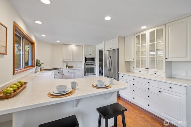 kitchen with a breakfast bar area, appliances with stainless steel finishes, glass insert cabinets, a peninsula, and a sink