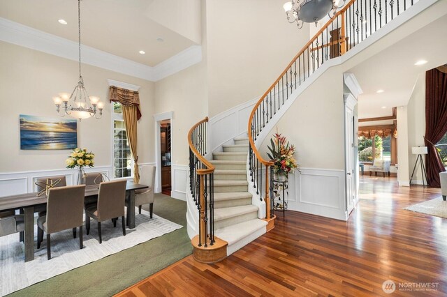 dining space featuring stairway, ornamental molding, wood finished floors, an inviting chandelier, and a decorative wall