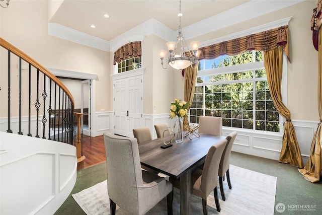 dining area with crown molding, a notable chandelier, a decorative wall, wainscoting, and stairs