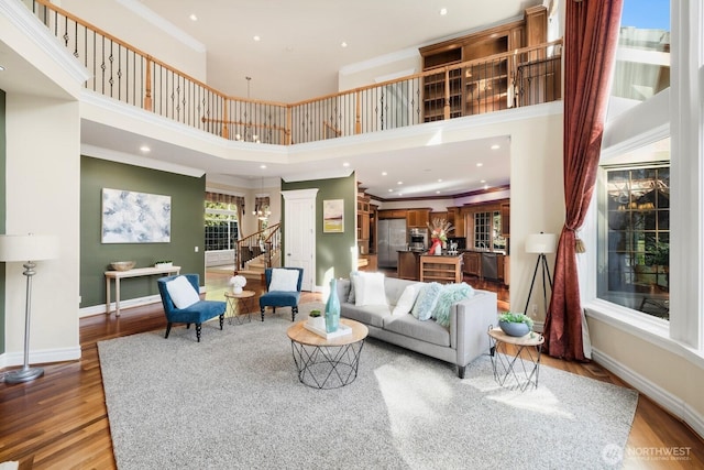 living area with baseboards, light wood-style flooring, ornamental molding, a high ceiling, and stairs