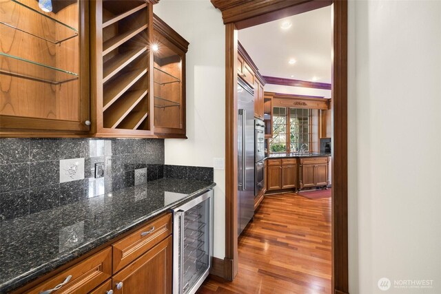 kitchen with dark wood-style flooring, brown cabinets, tasteful backsplash, dark stone countertops, and beverage cooler