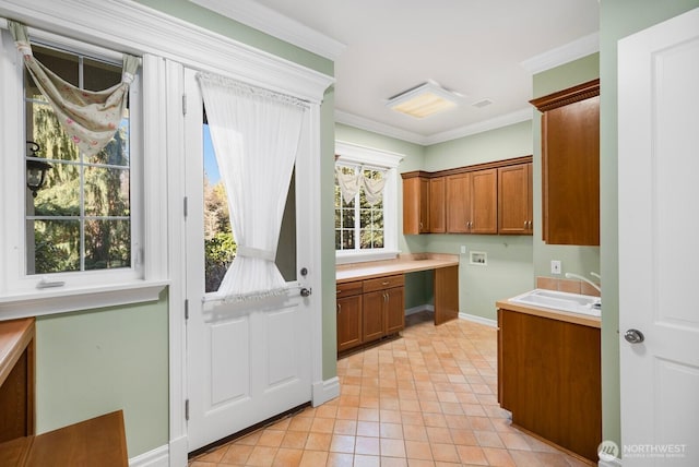 kitchen with a sink, light countertops, ornamental molding, built in study area, and brown cabinetry