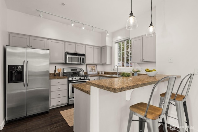 kitchen with dark wood finished floors, appliances with stainless steel finishes, gray cabinetry, a kitchen bar, and a sink