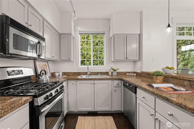 kitchen with a wealth of natural light, appliances with stainless steel finishes, dark stone counters, and a sink