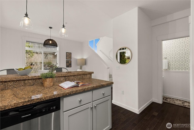 kitchen with baseboards, dark wood finished floors, dark stone countertops, hanging light fixtures, and stainless steel dishwasher