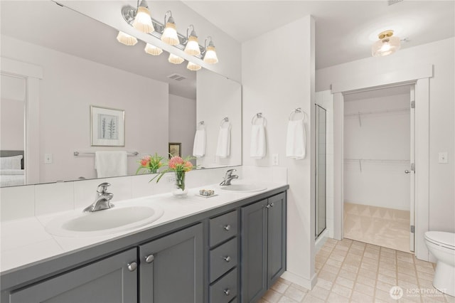 bathroom featuring visible vents, a sink, a shower stall, and double vanity