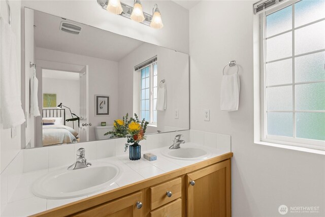 ensuite bathroom featuring double vanity, ensuite bath, visible vents, and a sink