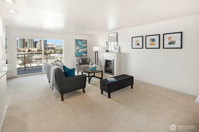 living room with a city view, recessed lighting, light colored carpet, baseboards, and a glass covered fireplace