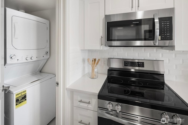 kitchen with stacked washer and clothes dryer, appliances with stainless steel finishes, light countertops, white cabinetry, and backsplash