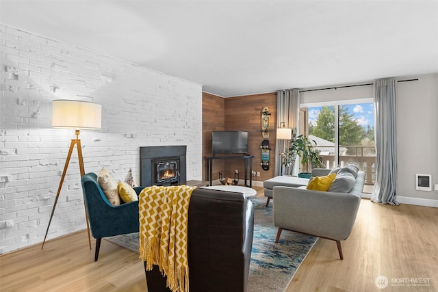 living room with a large fireplace, baseboards, brick wall, light wood-style flooring, and heating unit