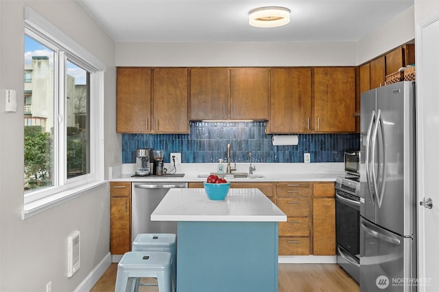 kitchen with decorative backsplash, appliances with stainless steel finishes, brown cabinets, light countertops, and a sink