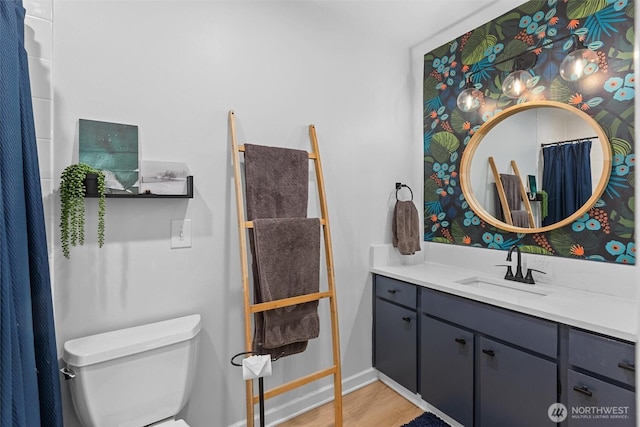 bathroom with toilet, wood finished floors, vanity, and baseboards